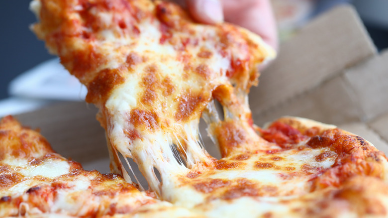 Hand picking up a slice of pizza with melted cheese