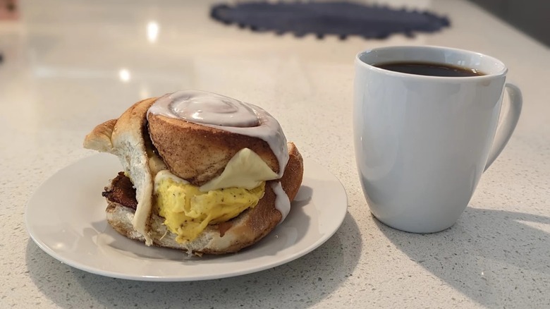 Cinnamon roll breakfast sandwich on a plate with a cup of coffee