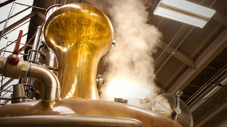 steam rising from an open hatch on a copper still