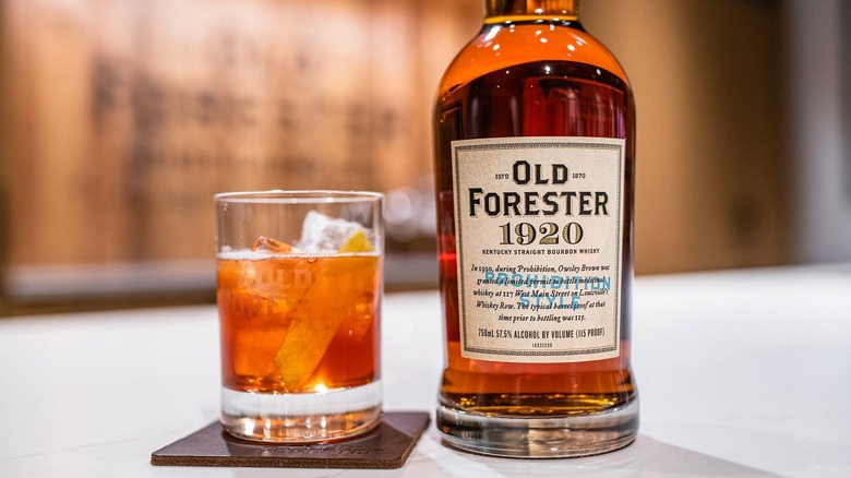 A close shot of a bottle of Old Forester 1920  next to a cocktail in a branded glass