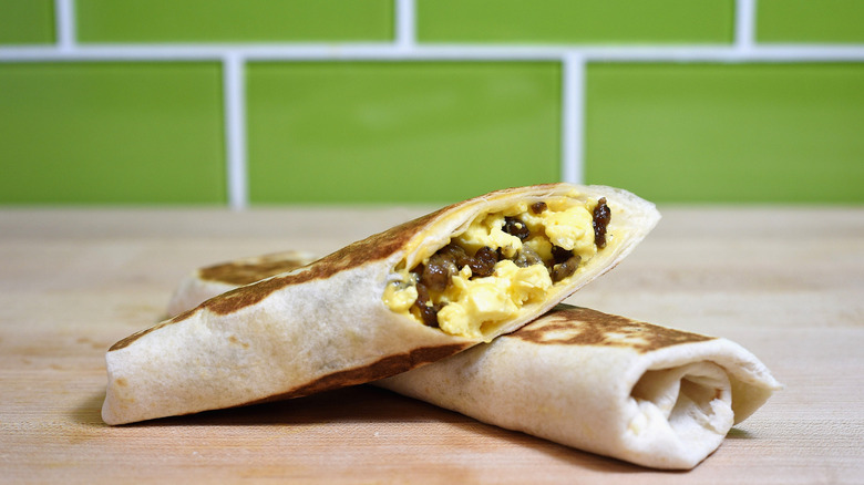 Two Taco Bell breakfast burritos on a counter, with one slice open to see inside