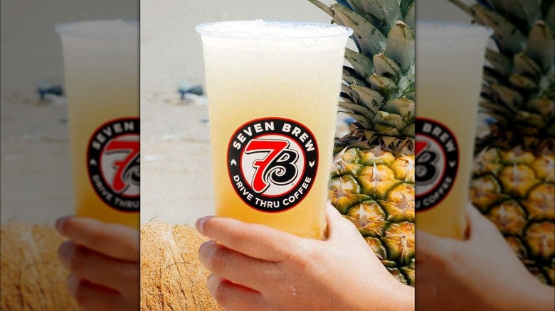 Hand holding 7 Brew Island Dream Lemonade Frozen Chiller drink with pineapple in background