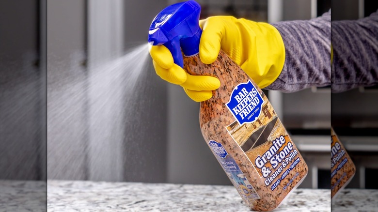 A person wearing yellow rubber gloves spraying Bar Keeper's Friend Granite & Stone Cleaner & Polish on a counter