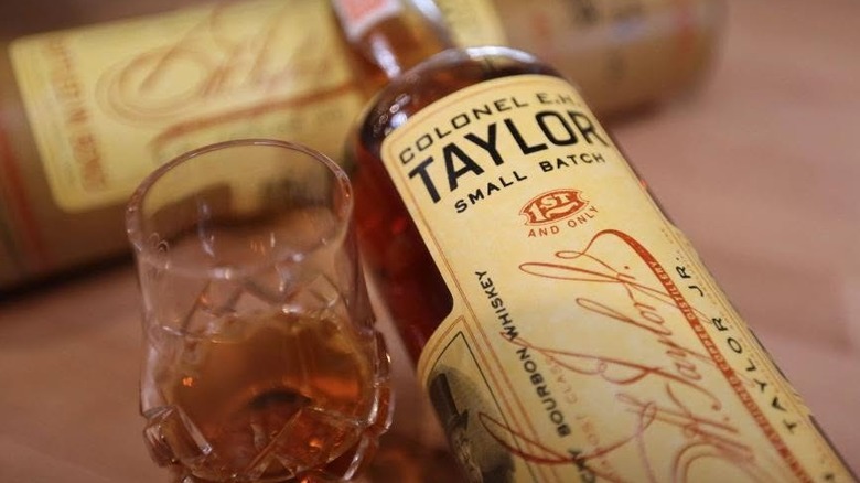 A close shot of a bottle of E.H. Taylor Small Batch resting on its packaging tube, next to a filled glass