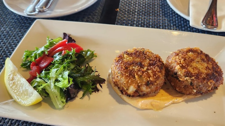Two crab cakes on plate with lemon wedge and greens