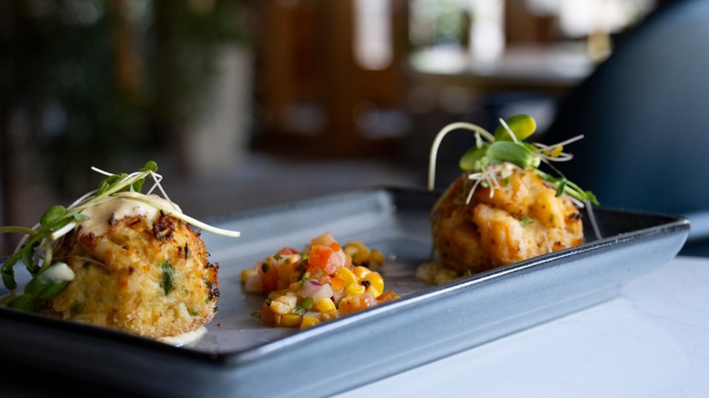 Two crab cakes with sauce, lemons, and lettuce