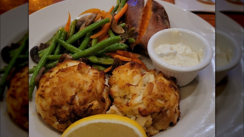 Two crab cakes with green beans, lemon, potato, and sauce