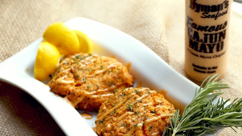 Two crab cakes on plate with lemon and rosemary with Cajun Mayo bottle