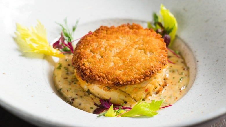 Crab cake in dish with sauce and greens