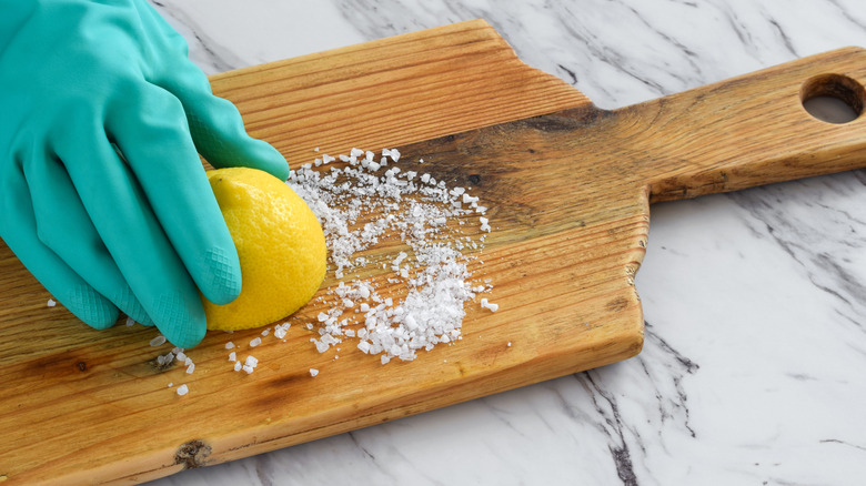 A gloved hand dabs half a cut lemon in salt on a chopping board