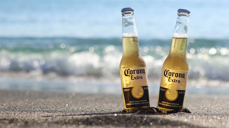 Two bottles of Corona Extra in the sand at the beach with waves breaking in the background