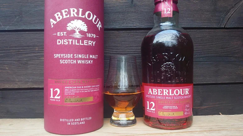 A bottle of Aberlour 12-year on a wooden surface next to its packaging and a filled glass