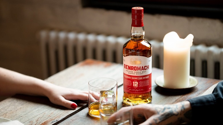 A bottle of Benromach 12-year on a table next to people with filled glasses