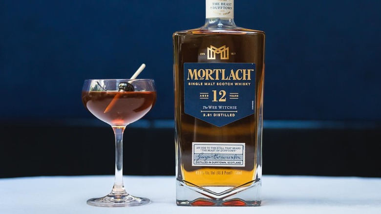 A bottle of Mortlach 12-year placed on a white table next to a cocktail