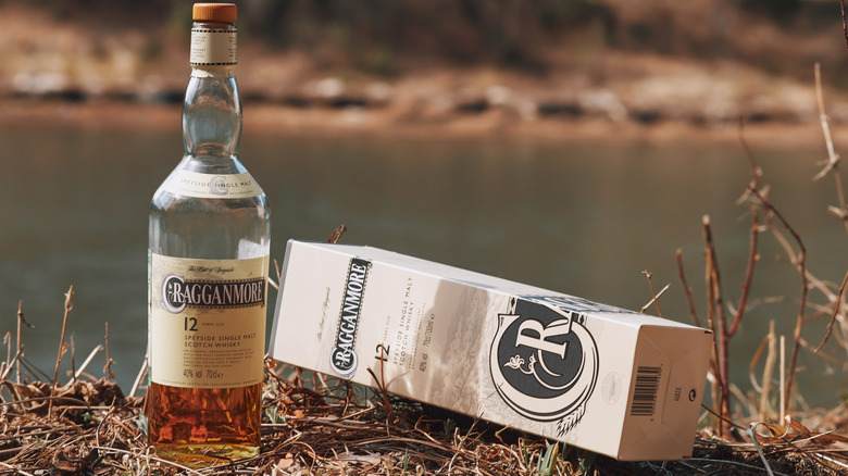 A half-empty bottle of the Cragganmore 12-year and its packaging on the bank of a river