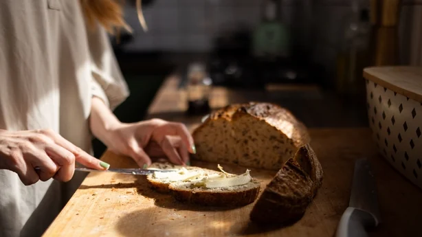 Woman spreading butter on a slice of whole wheat bread on a wooden cutting board