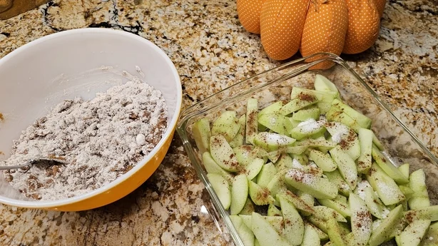 Slices of Granny Smith apples along with flour, nutmeg and cinnamon in a bowl, getting ready to mix ingredients for a delicious seasonal favorite dessert.