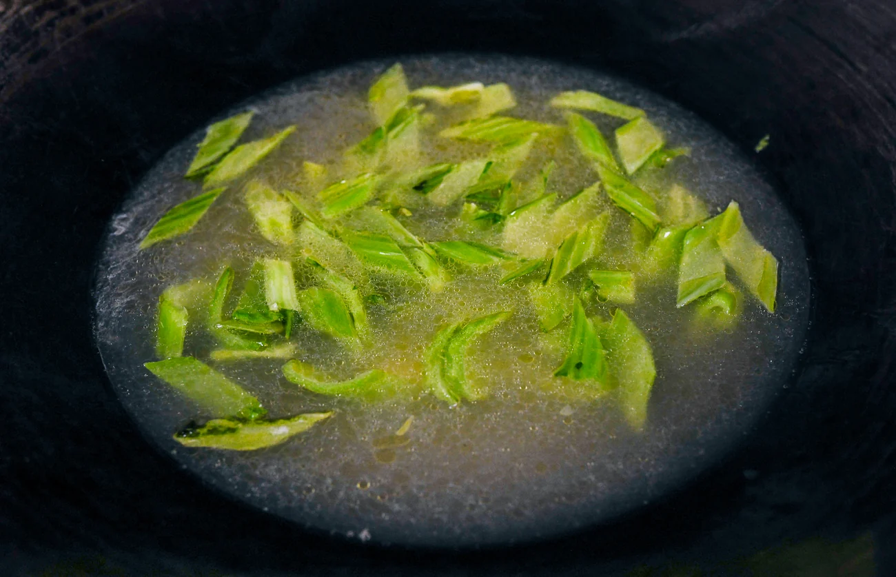 chicken stock added to mustard greens in wok