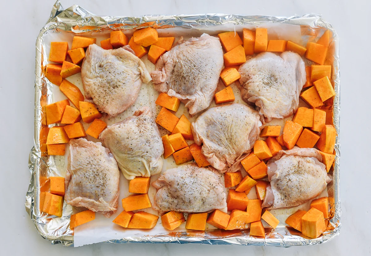 chicken thighs nestled into butternut squash on sheet pan