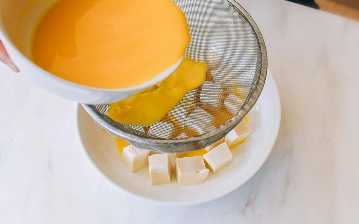 pouring beaten egg mixture through fine-mesh strainer over tofu