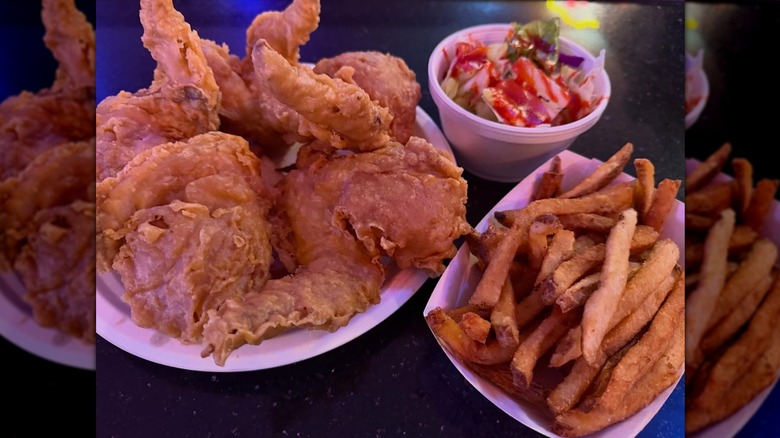 White plate of fried chicken next to small styrofoam bowl of salad and basket of fries