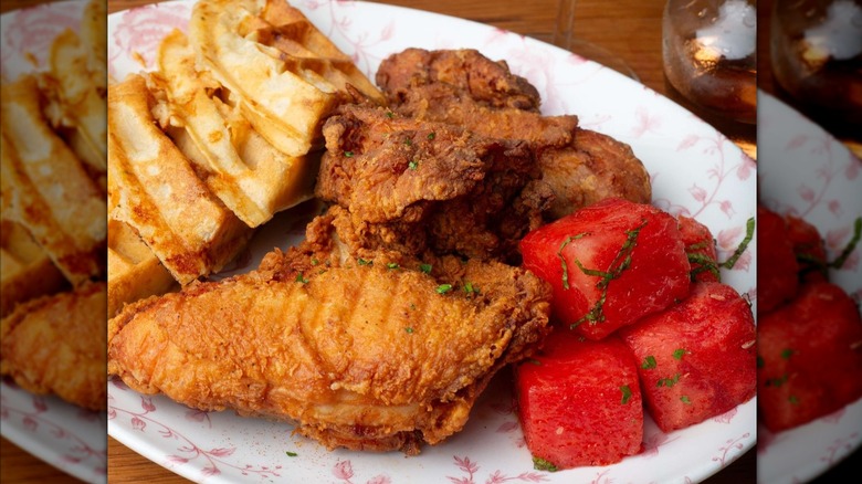 Fried chicken on pink floral plate next to waffles and watermelon