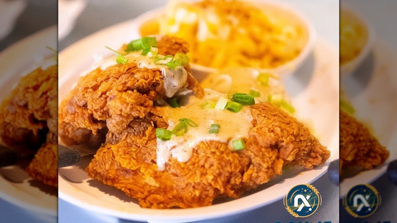 Fried chicken topped with gravy and green onions on white plate