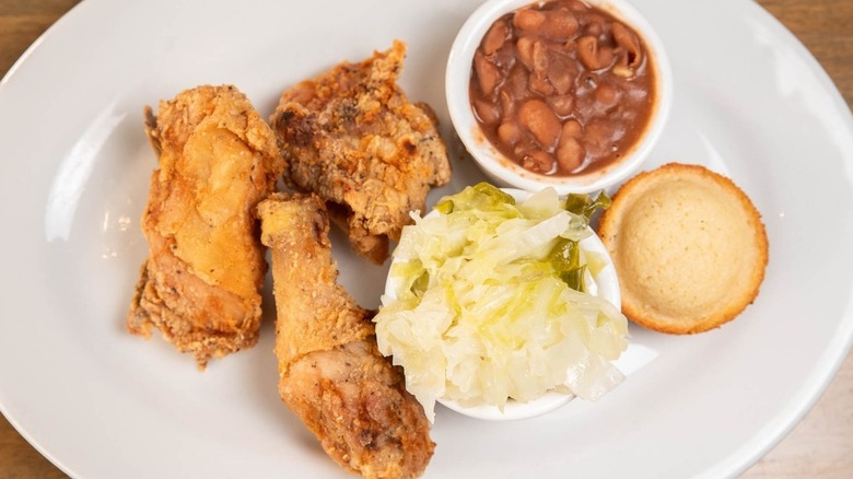 Top down shot of fried chicken pieces, cabbage, baked beans, and corn muffin on white plate