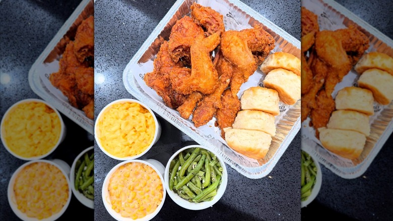 Top-down shot of aluminum tray of fried chicken and biscuits, next to cups of mac and cheese, creamed corn, green beans