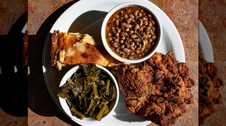 Top-down shot of white plate with fried chicken, buttered cornbread, beans, collards