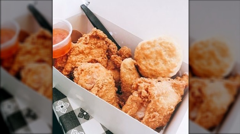 White box with fried chicken pieces, biscuit, and cup of sauce